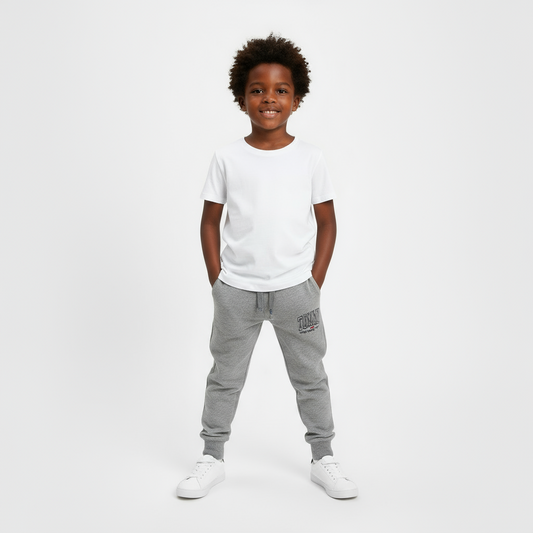 Four pairs of Tommy Hilfiger sweatpants in gray, navy, black, and red on a beige surface.